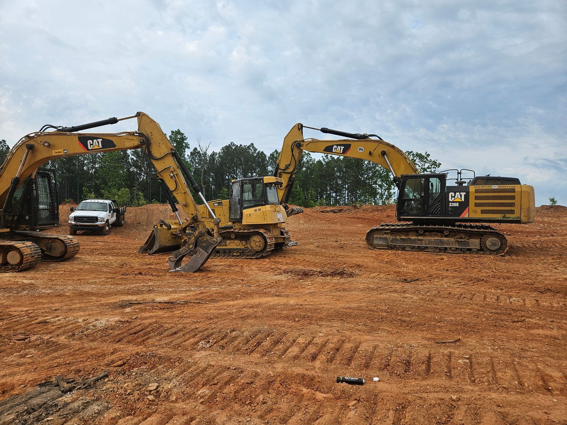 Three yellow Caterpillar excavators on a dirt construction site.