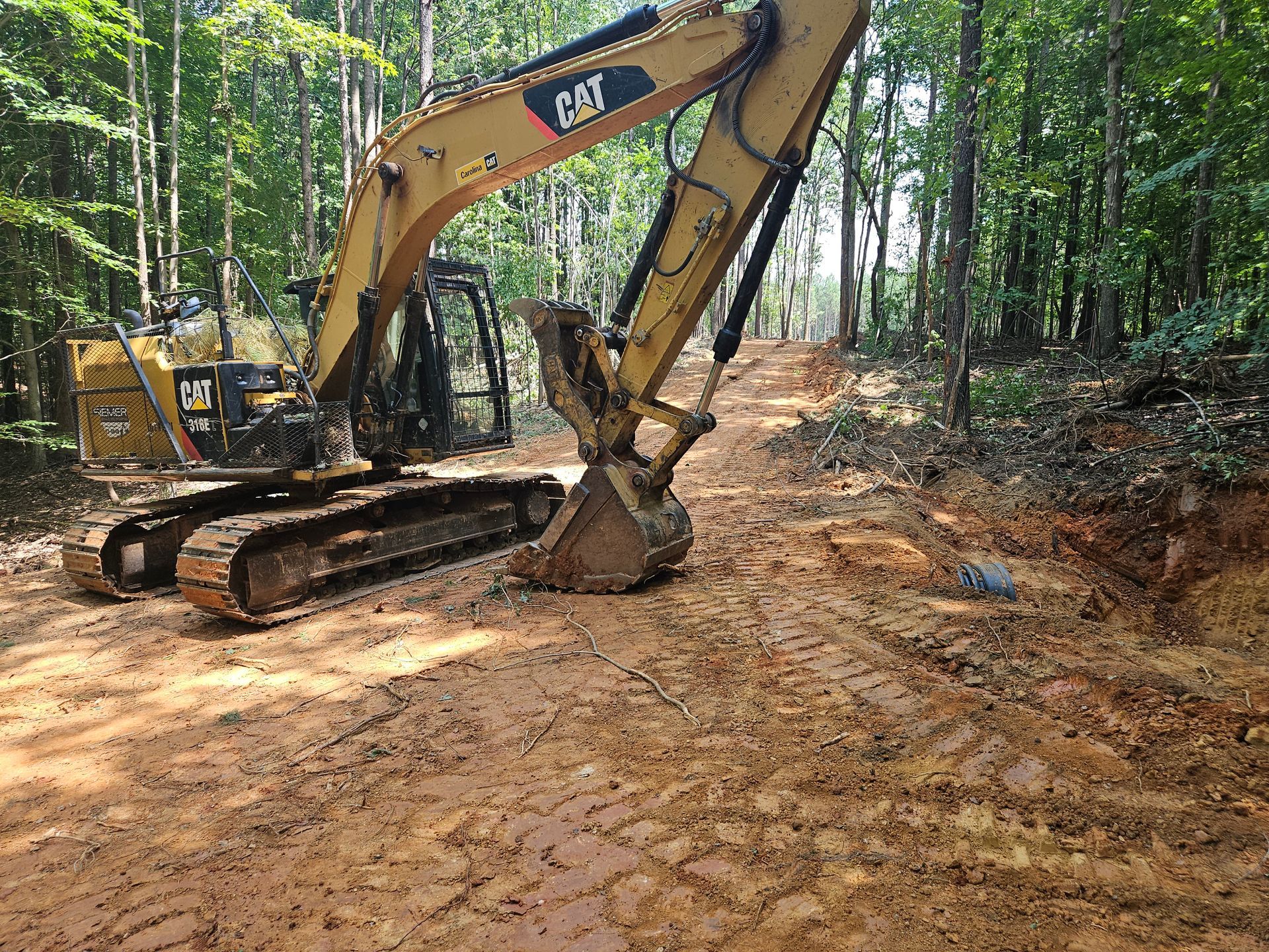 Yellow Caterpillar excavator clearing a muddy path in a wooded area.