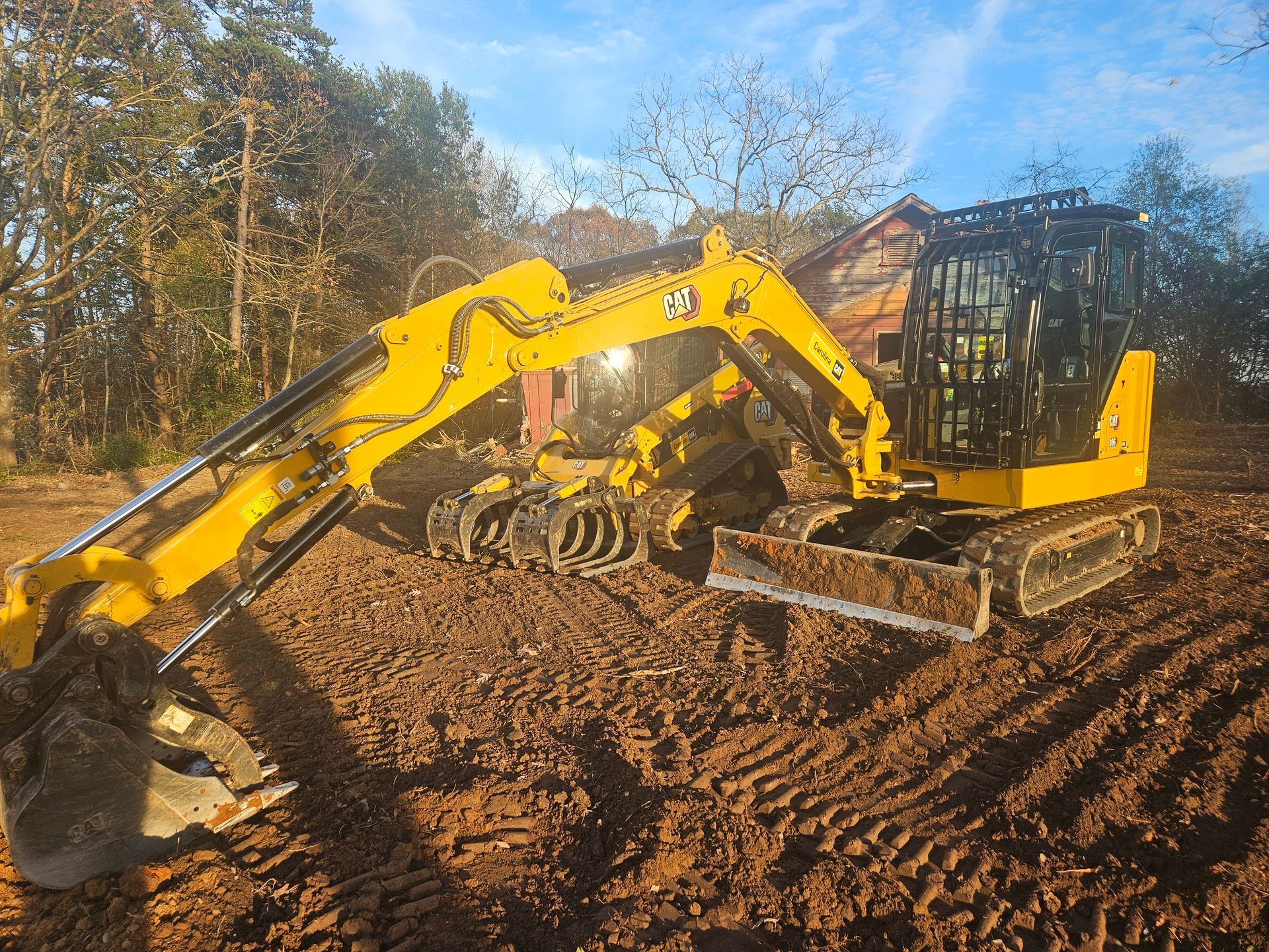 Yellow excavator on dirt, clearing a construction site with a structure in the background.
