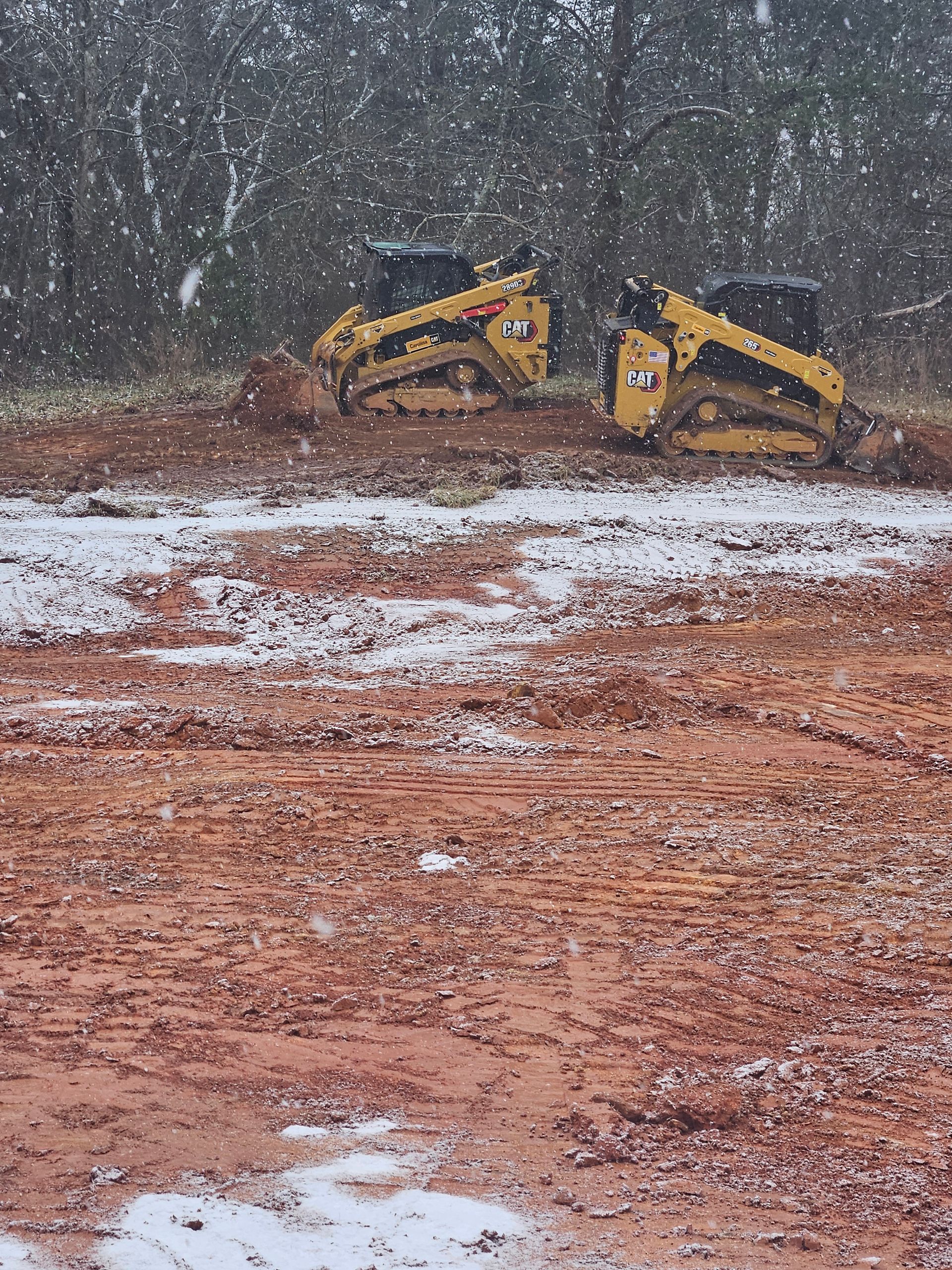 CAT excavator on a muddy dirt road in a forest clearing with another machine in the background
