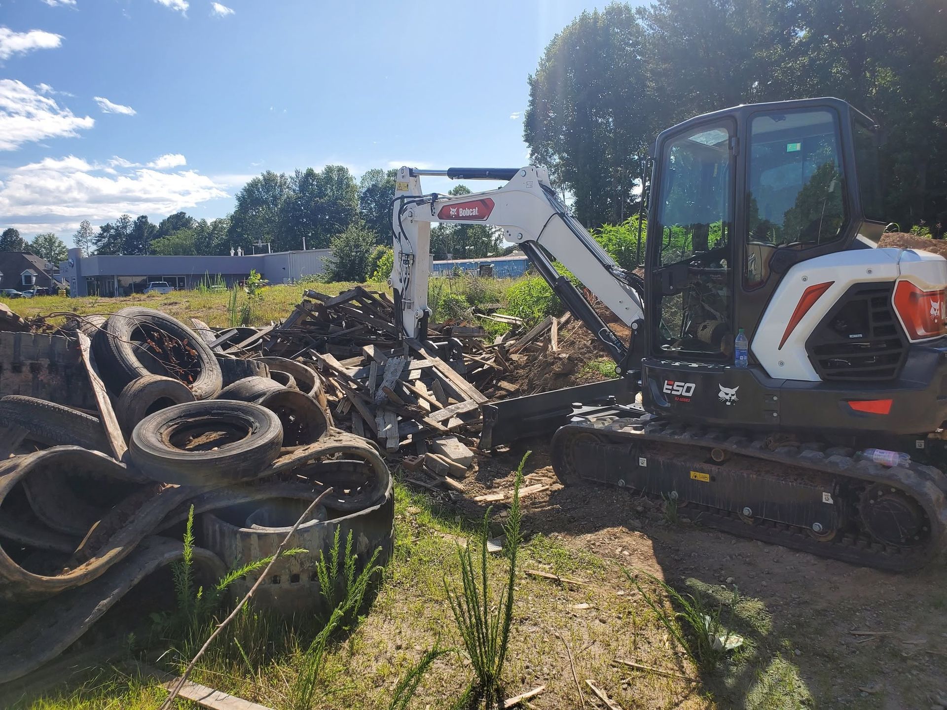Excavator lifting a pile of old tires and scrap in a sunny outdoor cleanup site