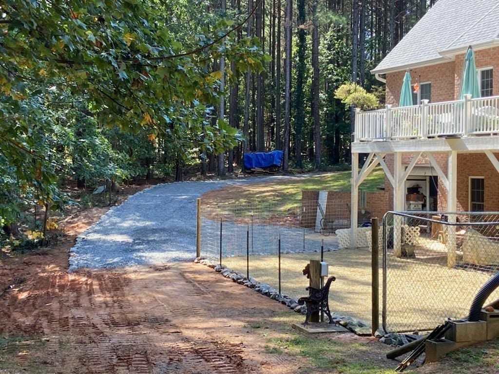Curved gravel driveway beside a house under construction, with a fenced yard and trees in the background