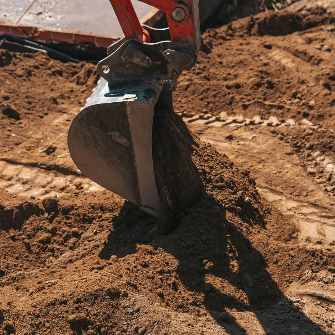 Excavator bucket digging into brown soil at a construction site