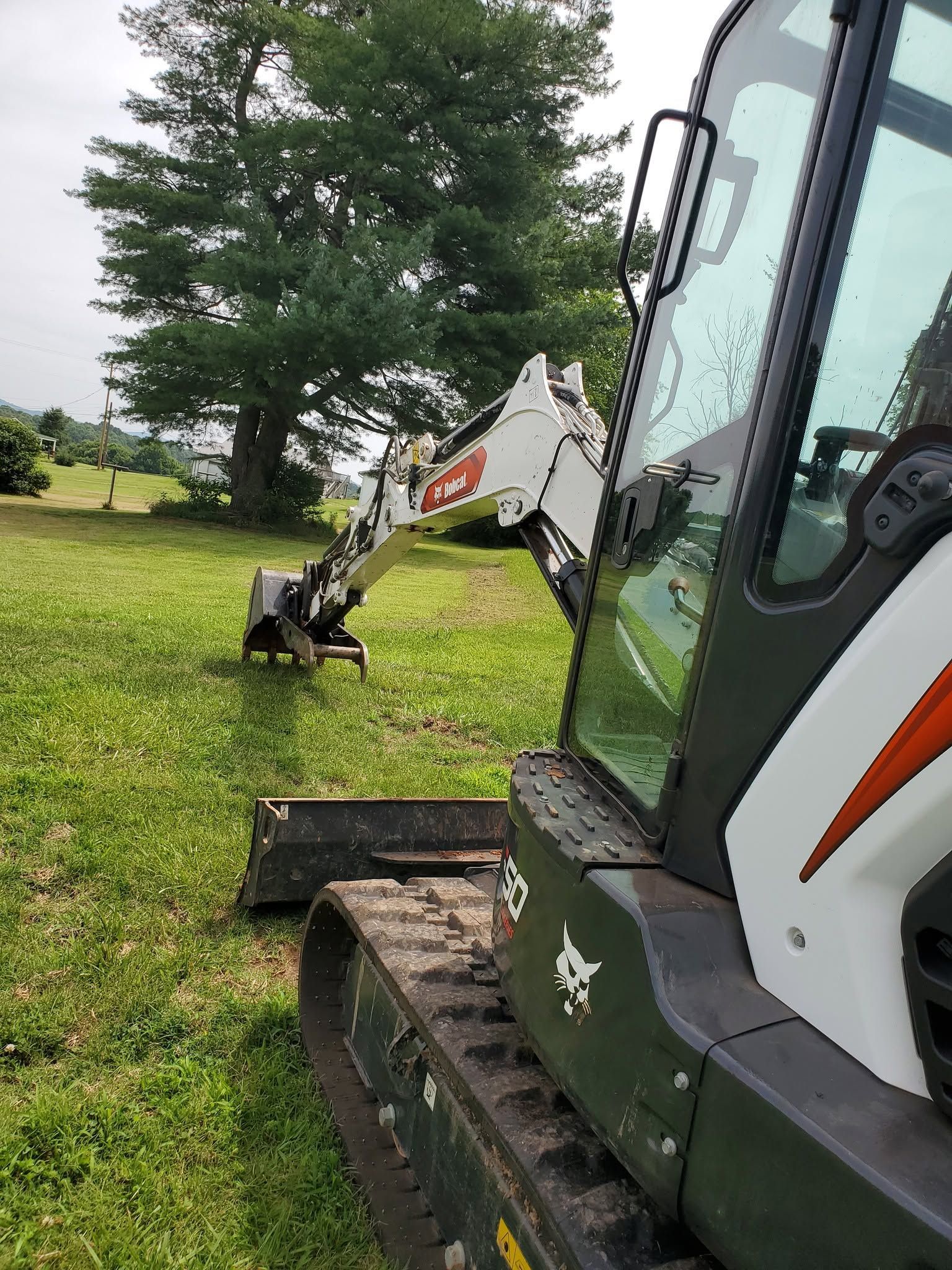 Compact excavator on grass near trees, white arm extended beside a black cab.