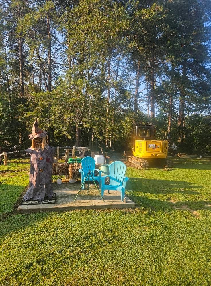 Backyard patio with blue chairs, a stone fire pit, and a yellow grill in front of tall trees