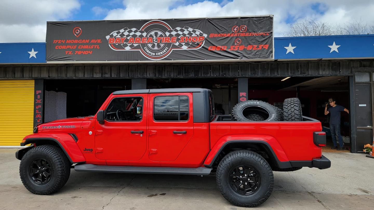 Red Jeep Gladiator pickup truck parked outside a shop, tires in the bed.