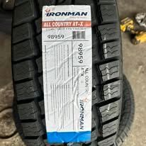 Close-up of a black Ironman All Country AT-X tire with a white label attached.