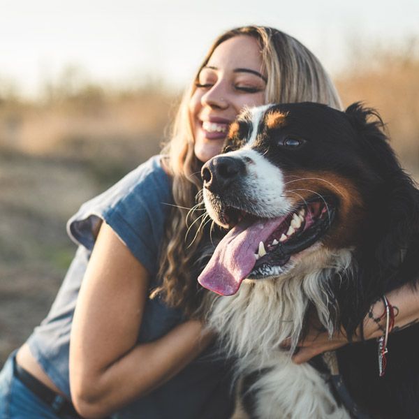 Woman hugging a black-and-white dog outdoors, both smiling in warm sunlight