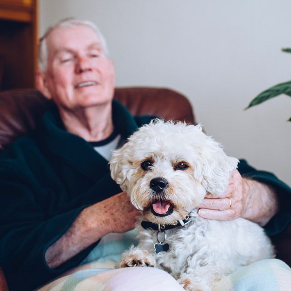 Older man seated indoors holding a fluffy white dog on his lap