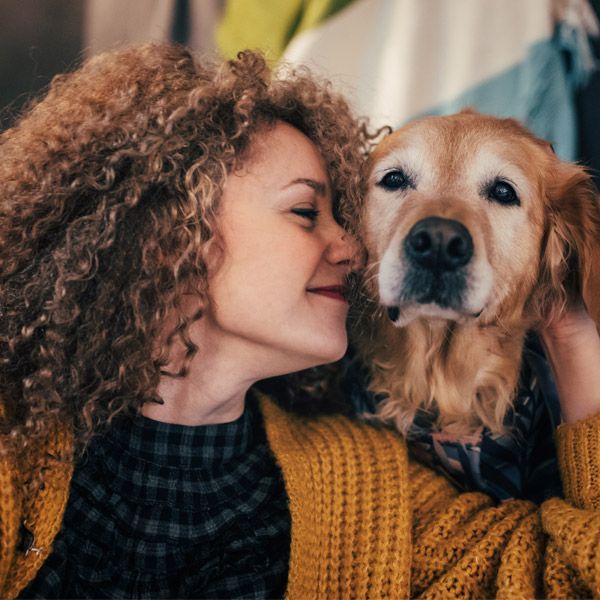 Woman in mustard sweater nuzzles a golden dog indoors