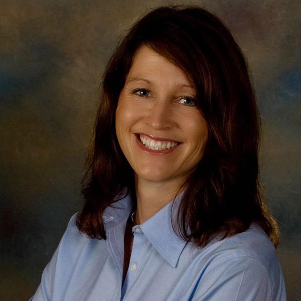 Smiling woman in a light blue shirt posed against a gray studio backdrop