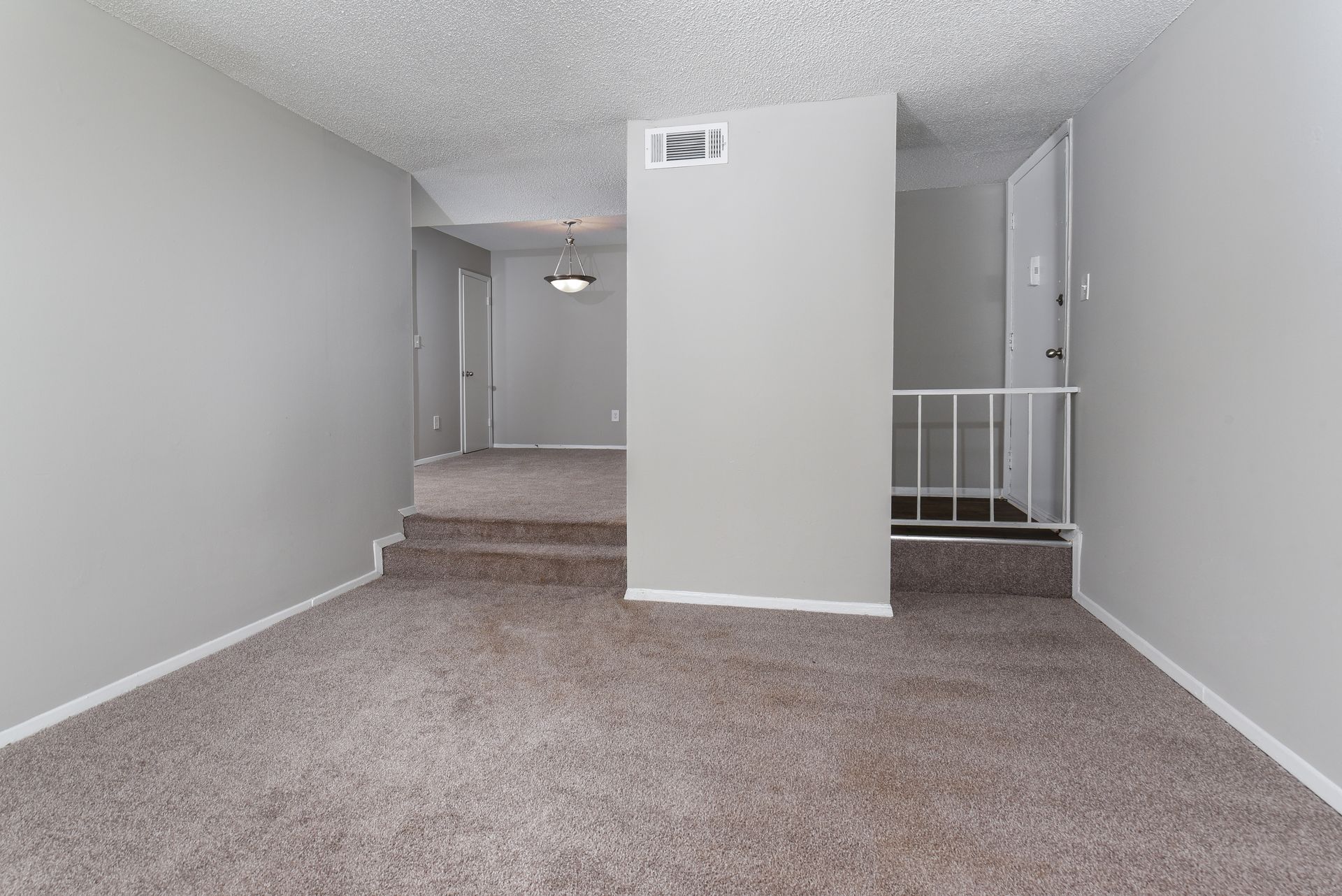 A split-level room with gray walls and carpet, featuring a central wall partition and steps leading to an upper area.
