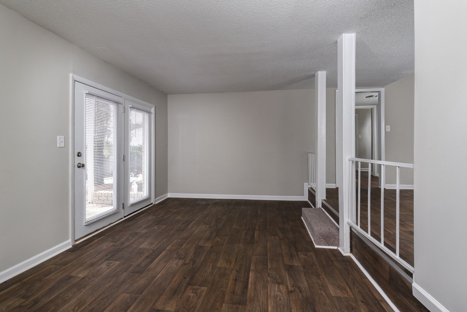 An interior view of a room with dark wood floors, light grey walls, white French doors, and a staircase with a railing.