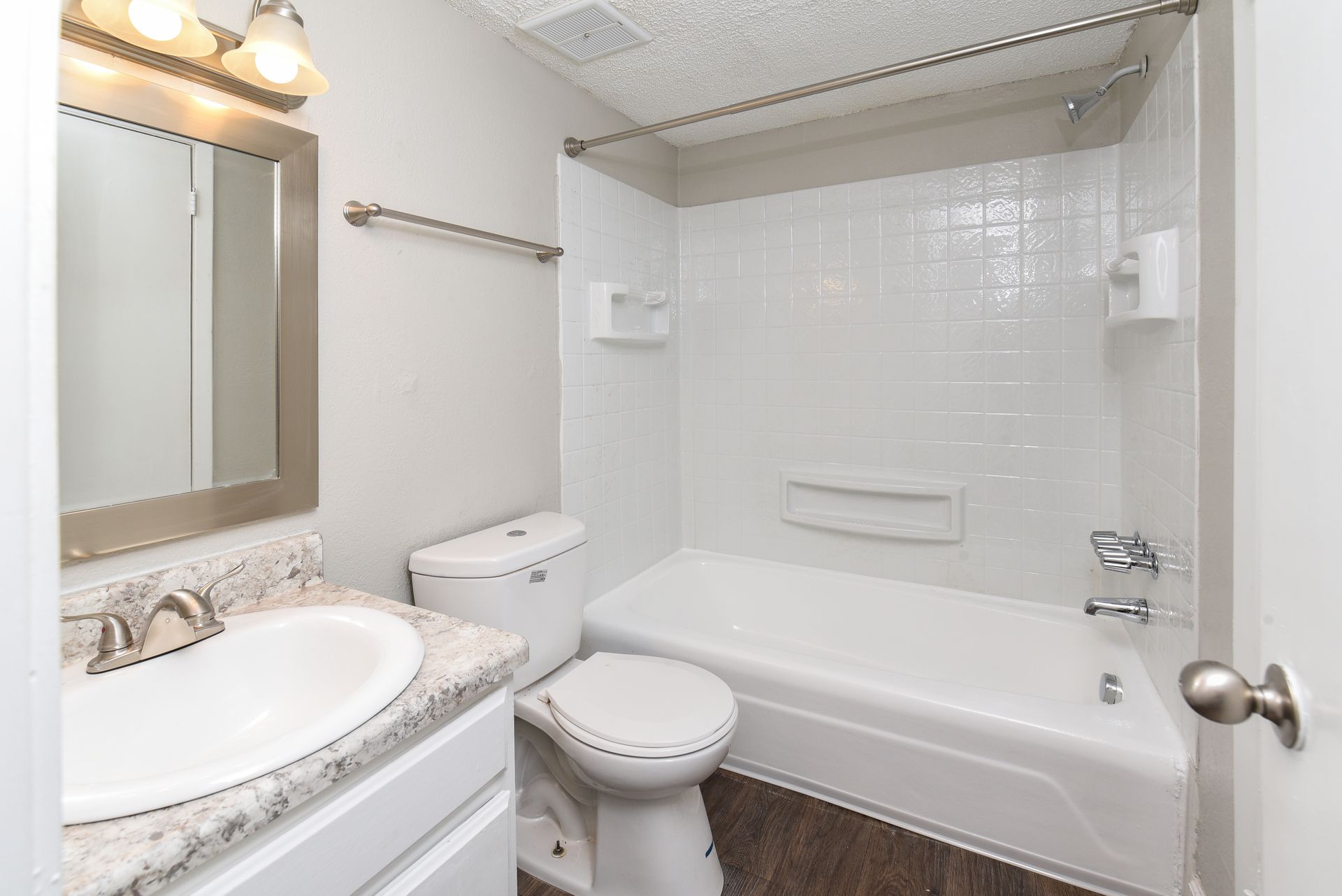 A bathroom featuring a white vanity with a speckled countertop, a toilet, and a shower-tub combination with white tiles.