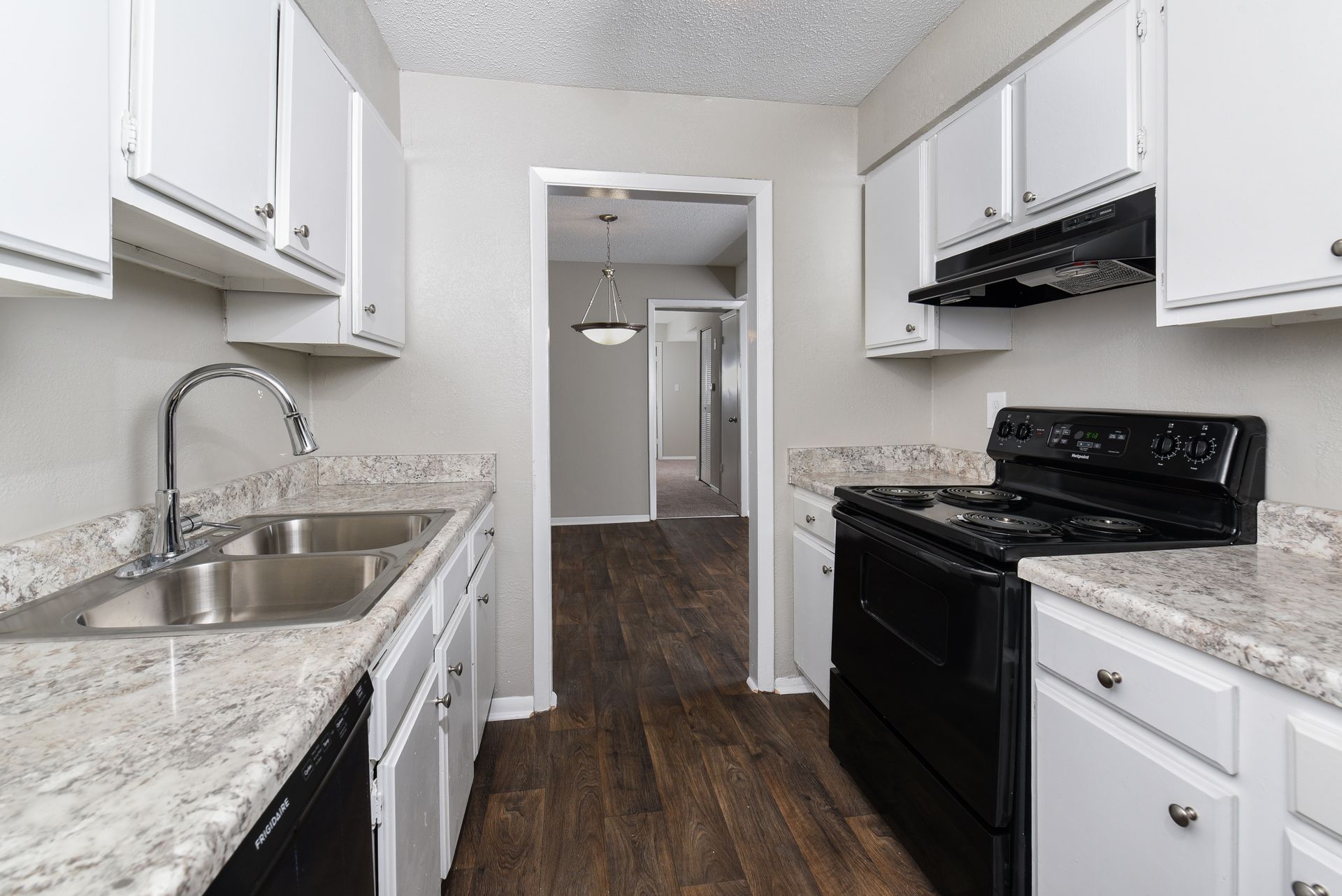 Galley-style kitchen featuring white cabinets, speckled countertops, black appliances, and a view into a dining area.