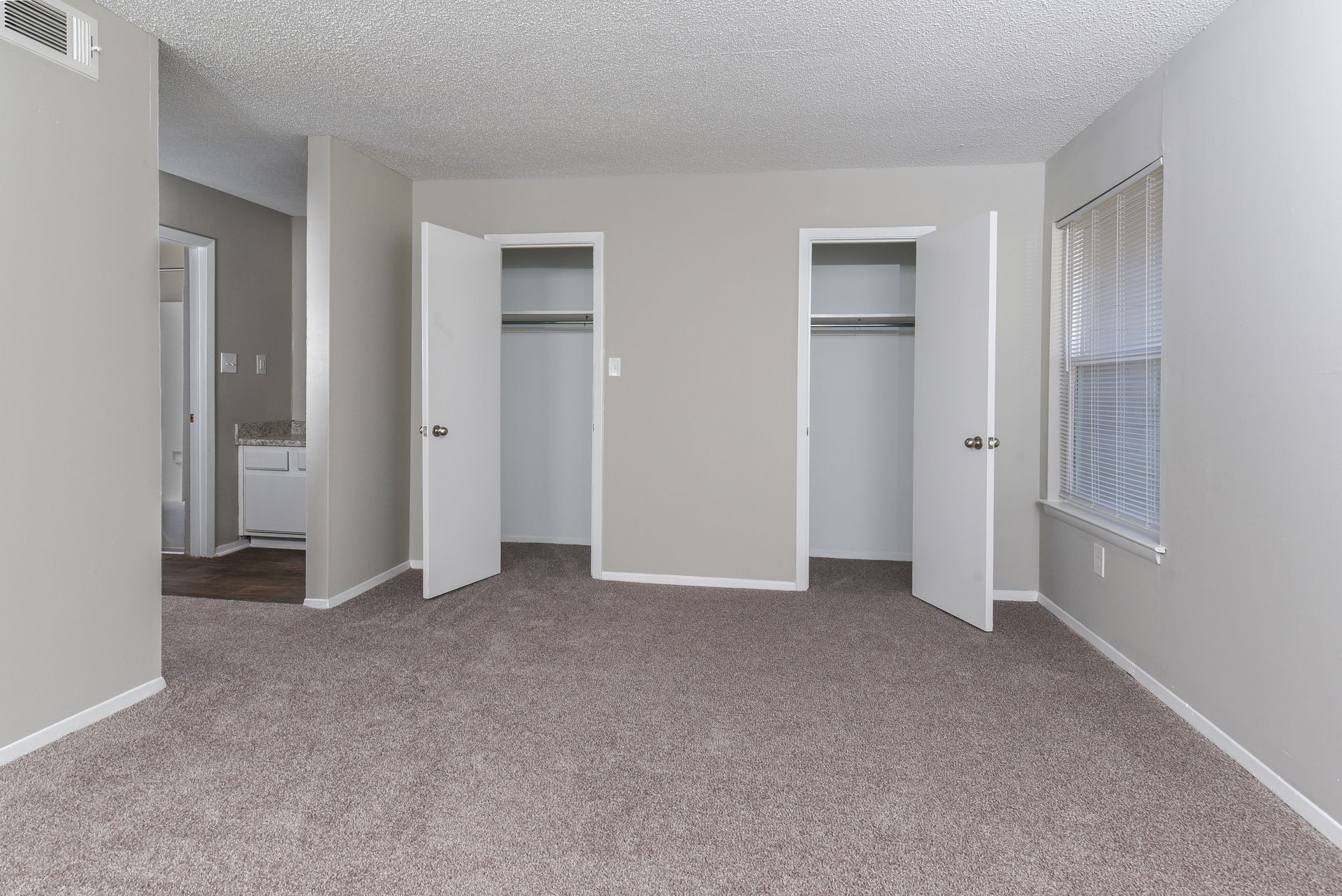 A carpeted bedroom with light gray walls, two open closet doors, and a doorway leading to a bathroom.
