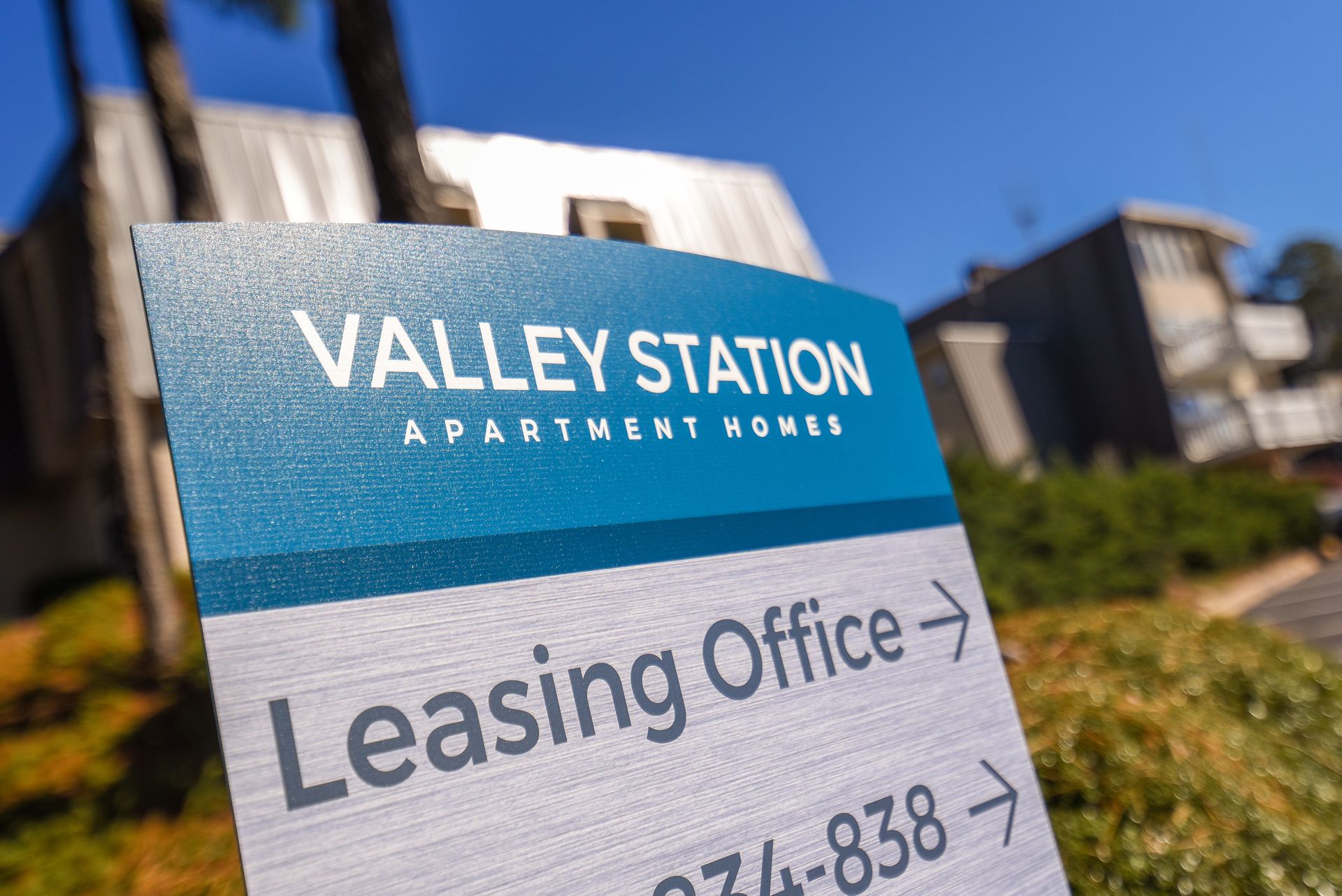 A Valley Station Apartment Homes sign featuring a blue and white directional sign pointing toward the leasing office.