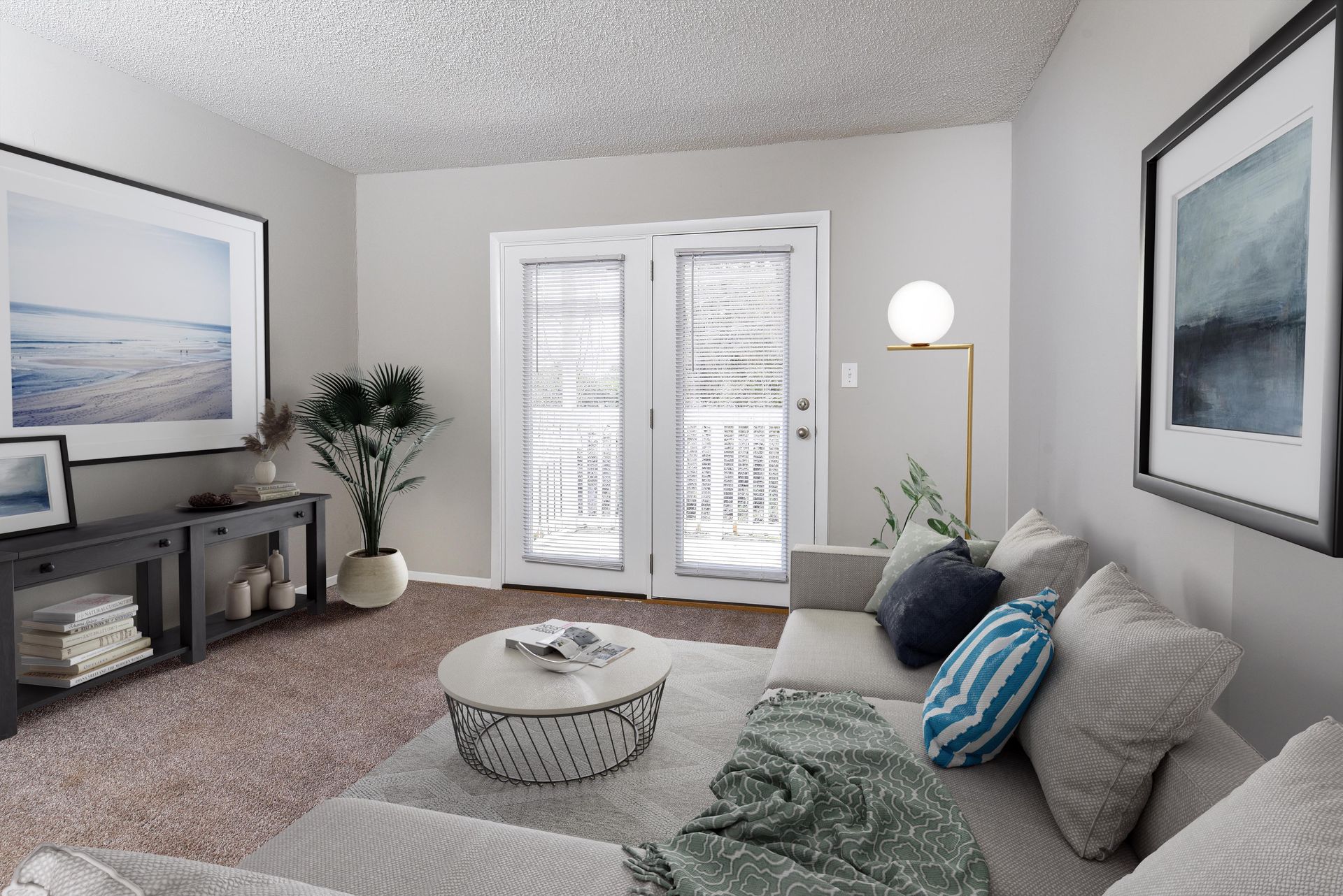A cozy living room with a gray sectional sofa, round coffee table, console table, artwork, and white double doors.
