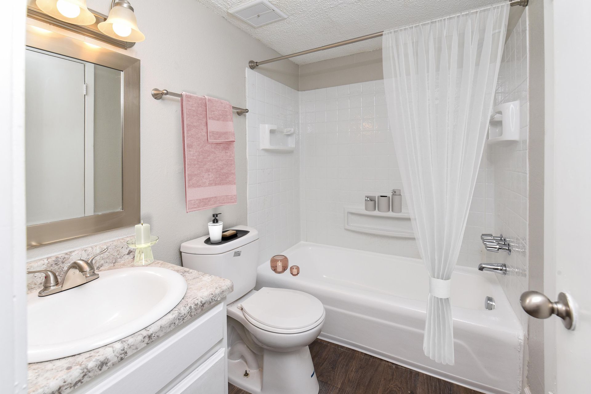 A bathroom featuring a white vanity with a speckled countertop, a toilet, and a bathtub with a white shower curtain.
