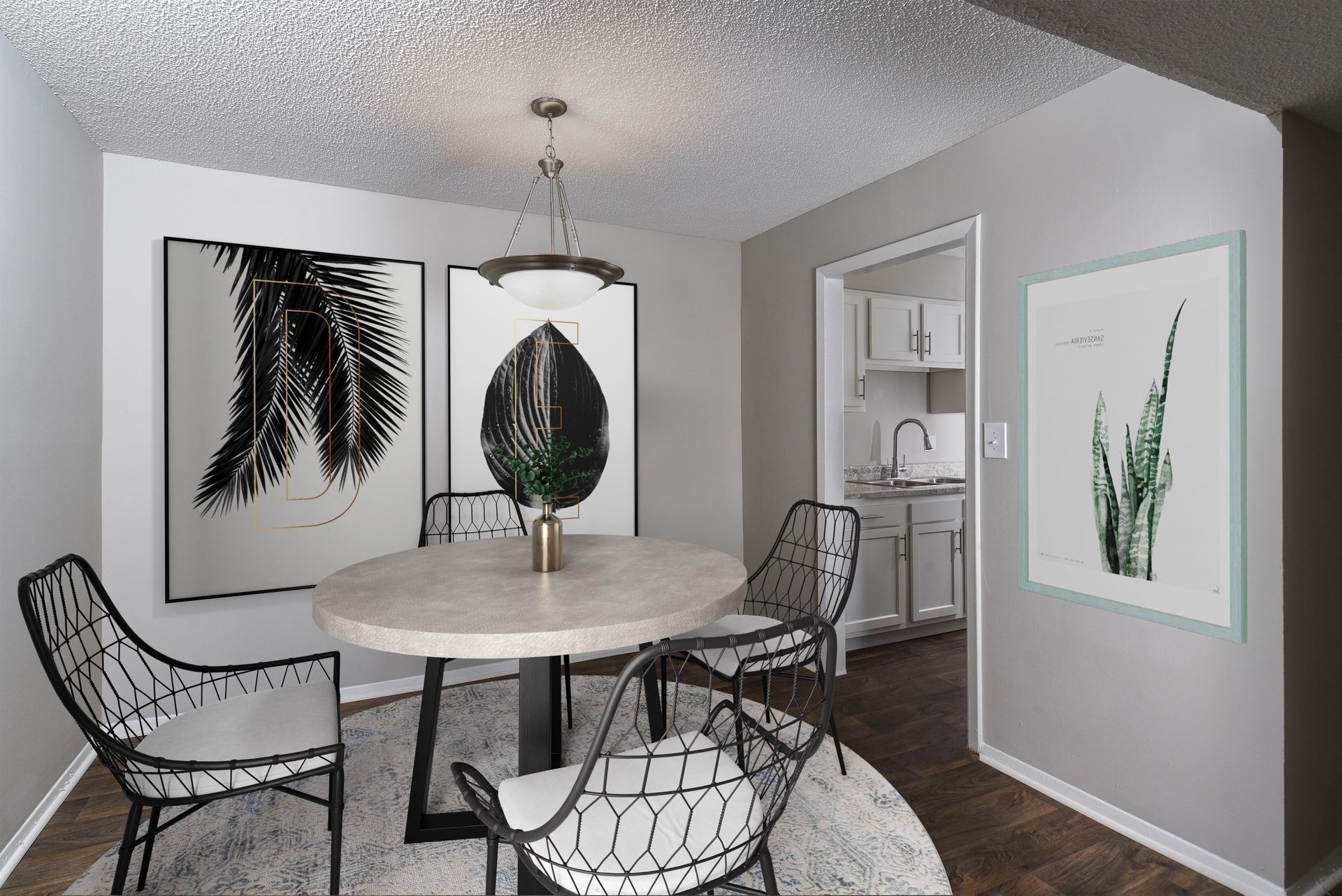 A dining area featuring a round stone table, four black metal chairs, a textured rug, pendant light, and framed artwork.