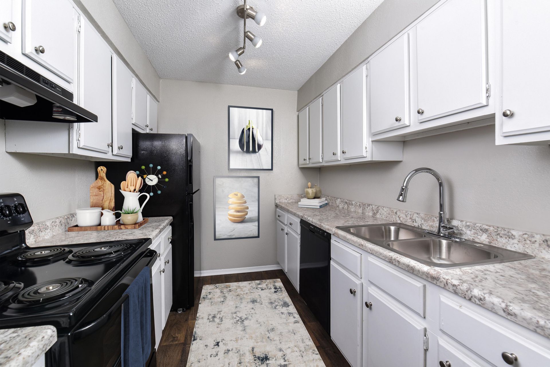 A modern galley kitchen featuring white cabinets, gray patterned countertops, a black stove, refrigerator, and rug.