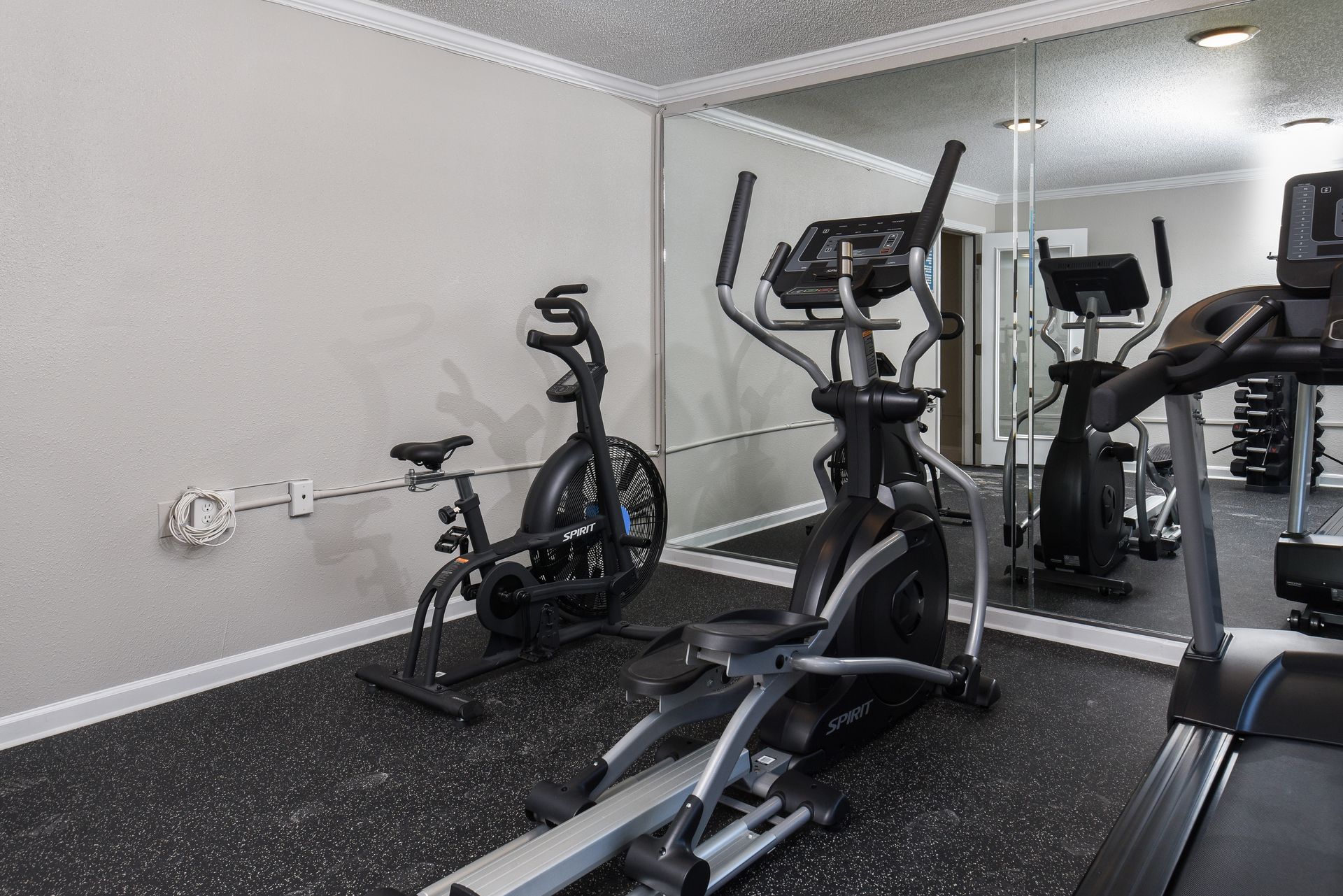 A home gym features an exercise bike and an elliptical machine positioned in front of a wall-length mirror.