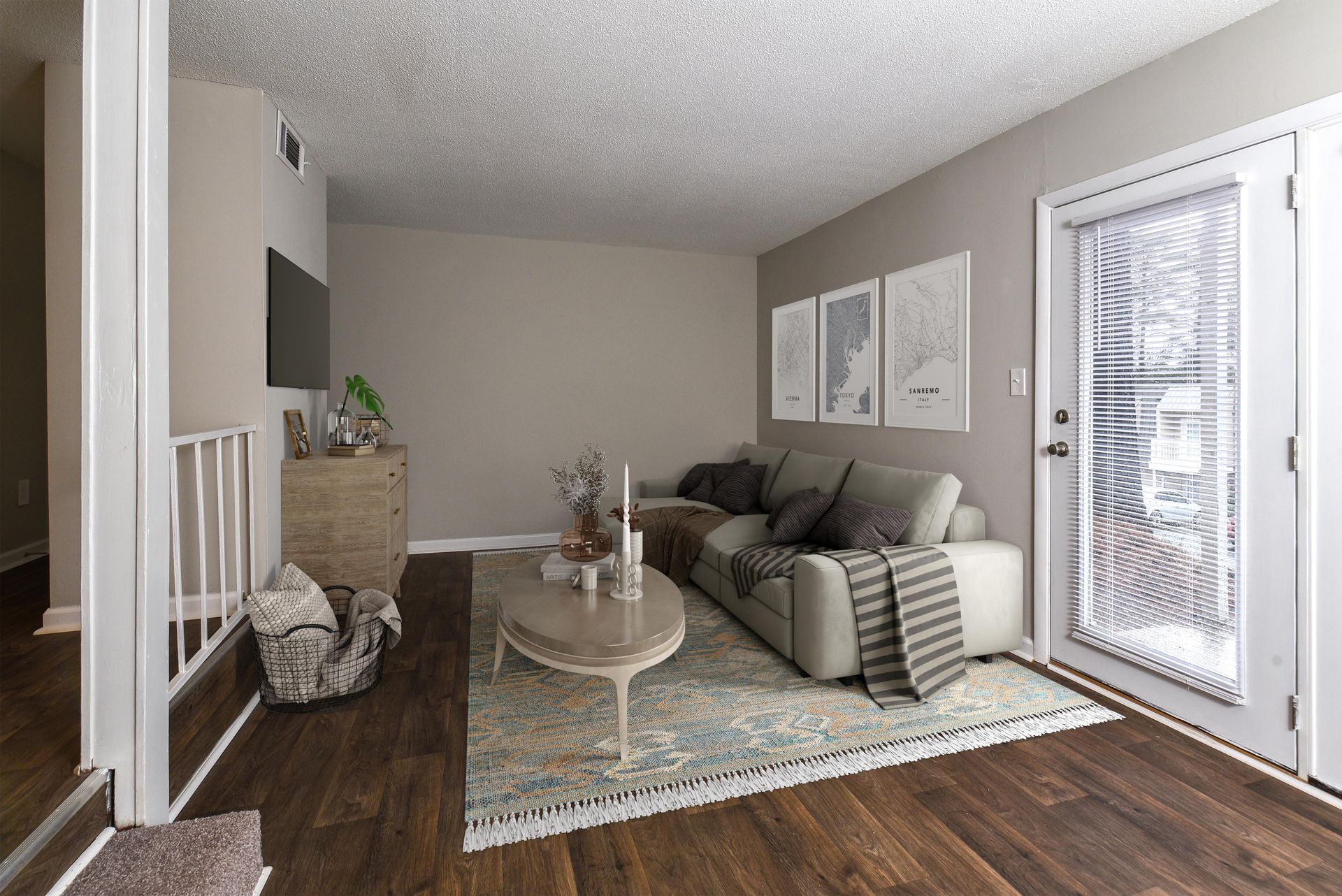 A cozy living room with a beige sofa, patterned rug, wooden coffee table, dresser, and wall art near a glass door.