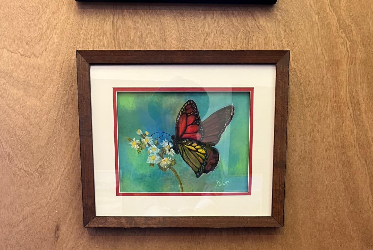 Framed butterfly artwork on a wood wall, with blue-green background and small flowers