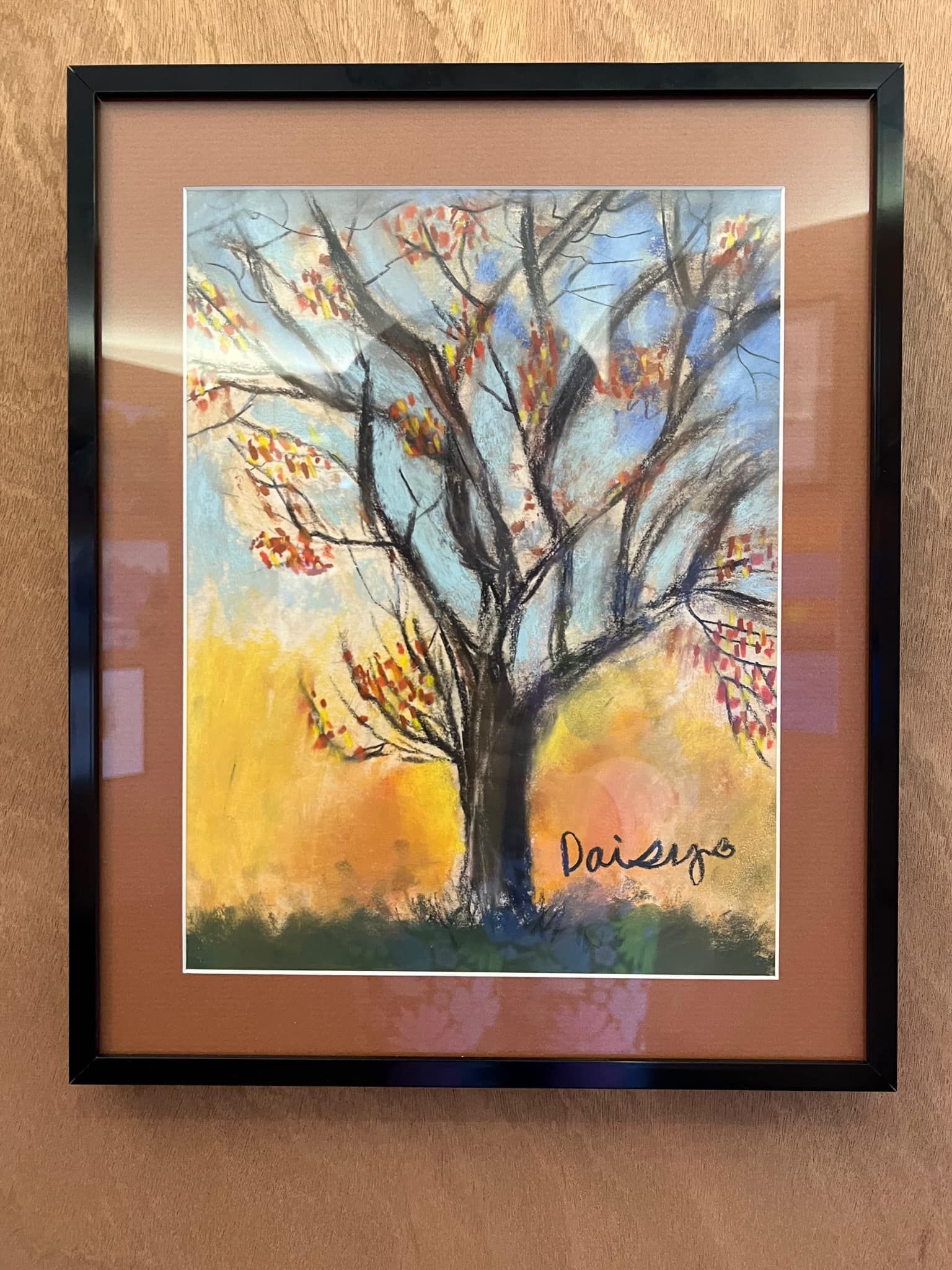 Framed watercolor painting of a tree with blue and yellow tones on a tan wall