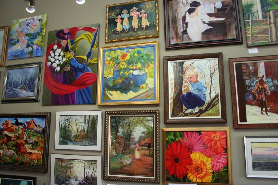 Assorted framed paintings and photos displayed on a wall, featuring colorful flowers, landscapes, and portraits