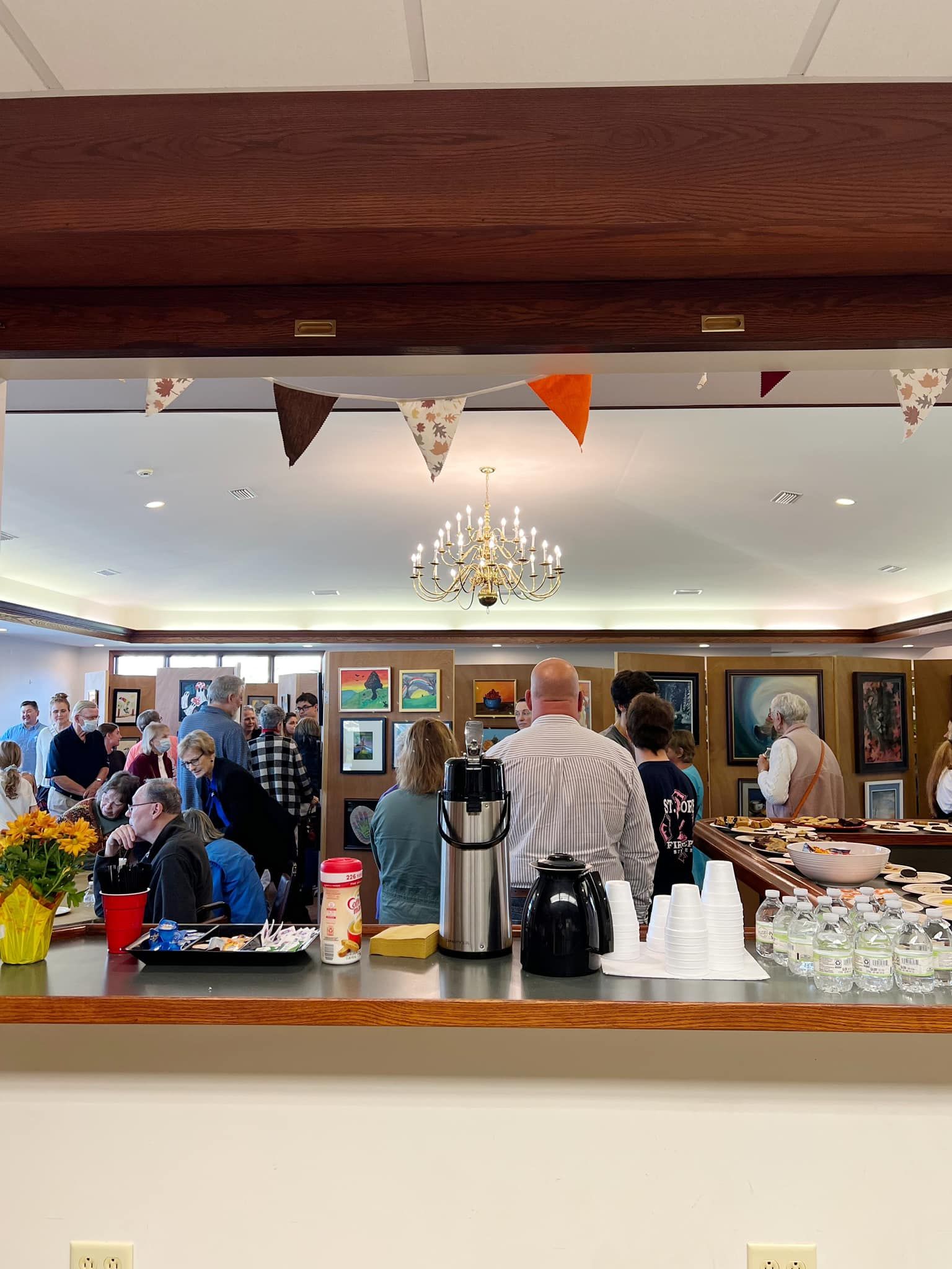Coffee and pastries at a bright café counter with bunting, chandelier, and people chatting in the background