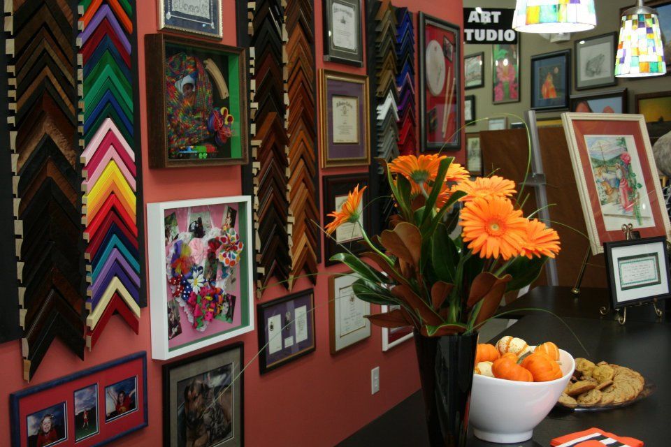 Colorful art display wall with framed artwork, chevron textiles, and a vase of orange flowers beside fruit bowls
