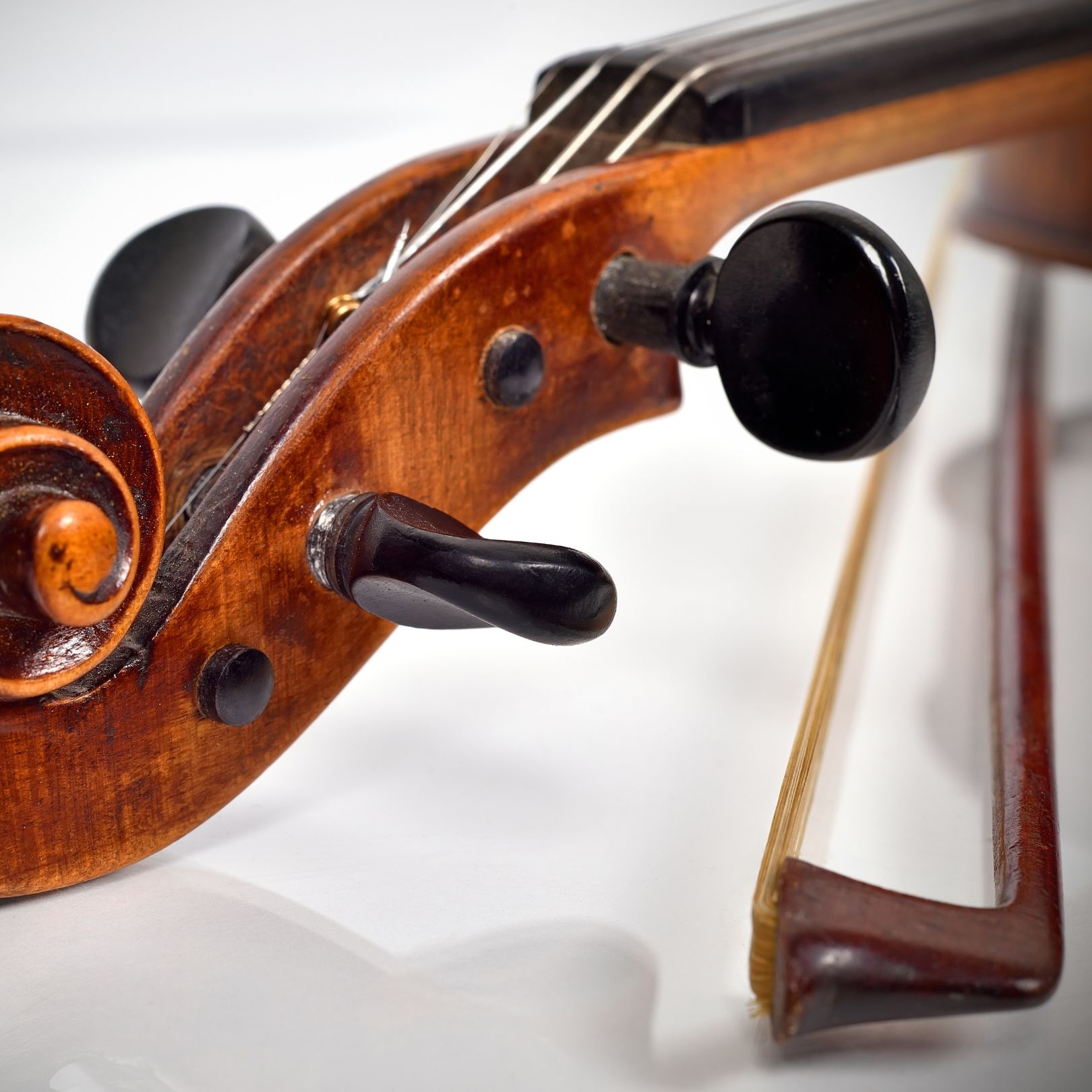 Close-up of a violin scroll and tuning pegs with a bow resting beside it