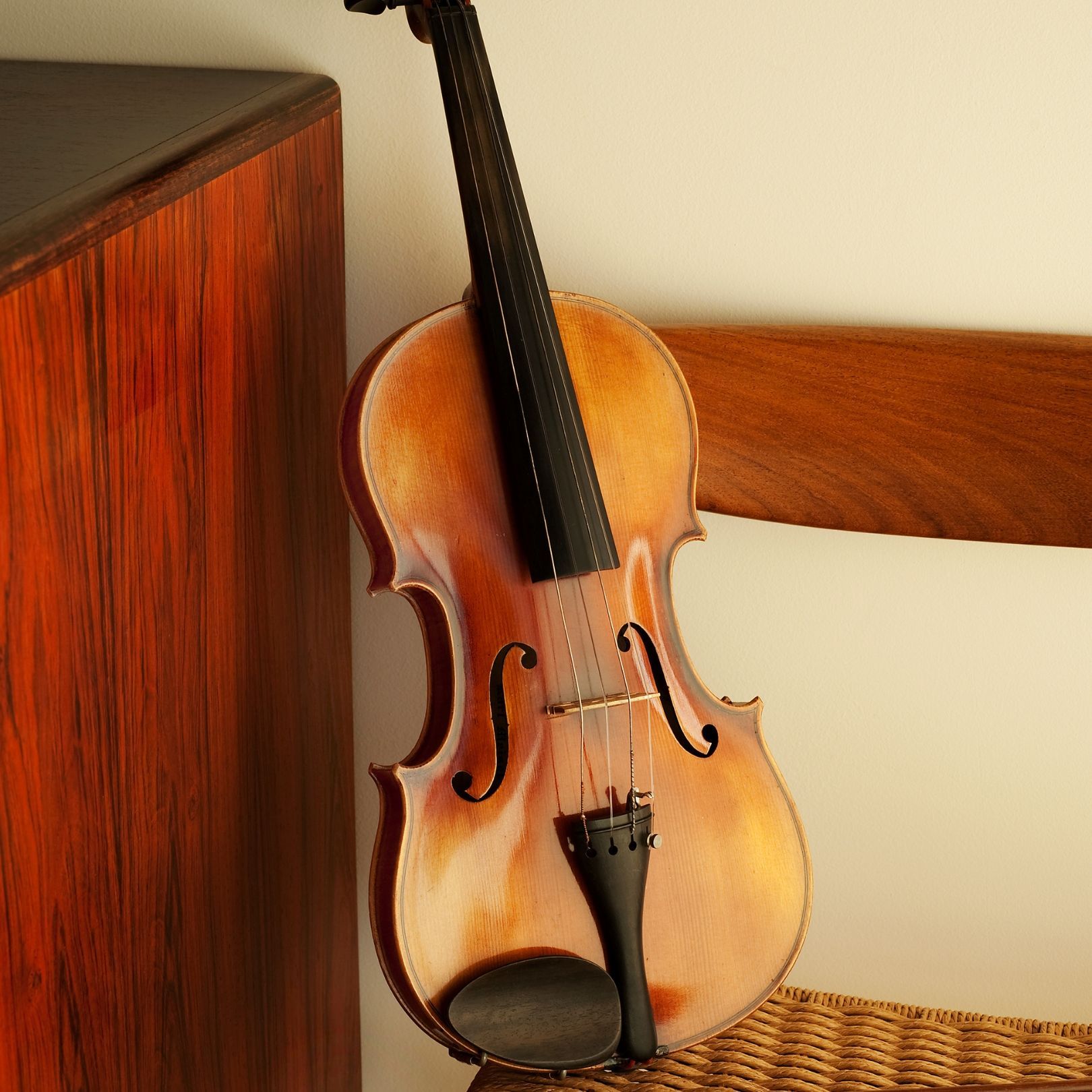 Violin with a warm brown finish leaning against a chair and wooden wall panel