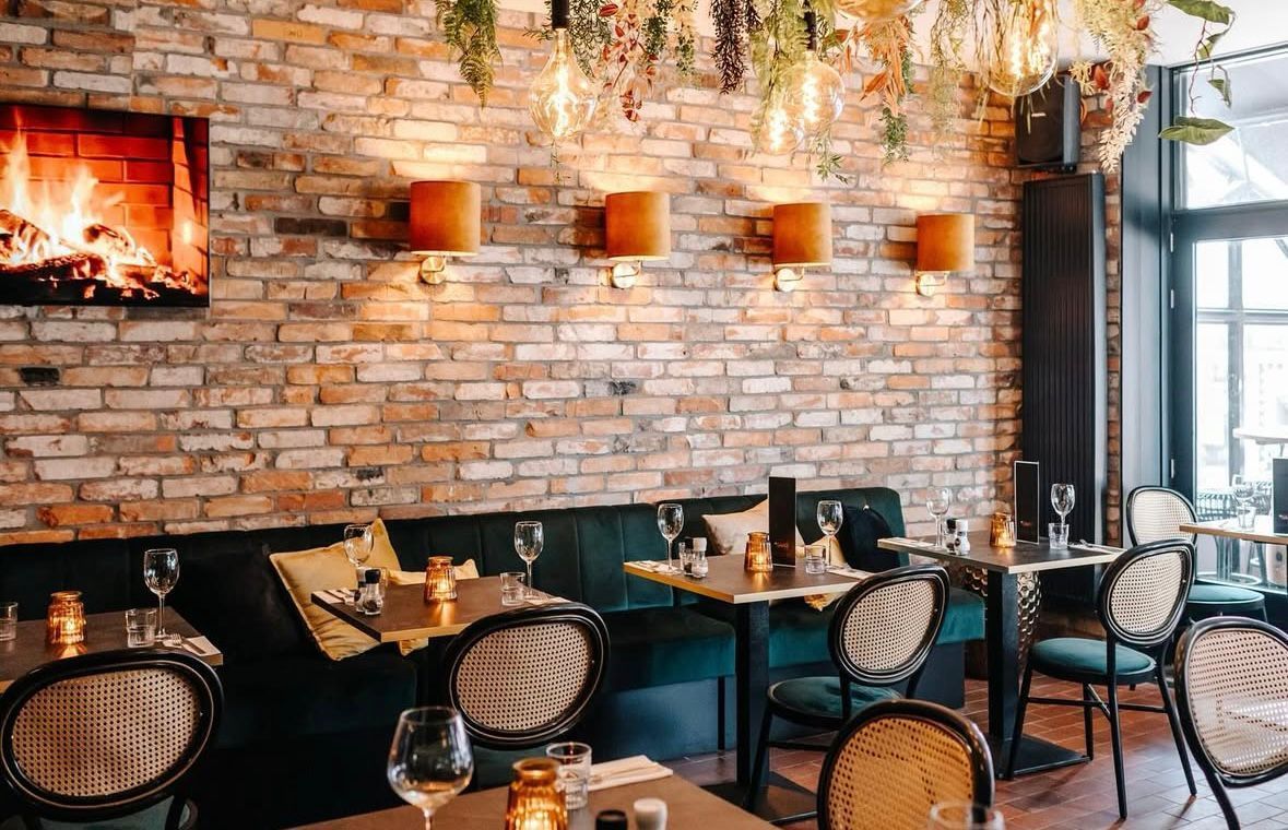 Gezellig restaurant met bakstenen muren, hanglampen, zwarte tafels, gevlochten stoelen en een sfeervolle open haard.