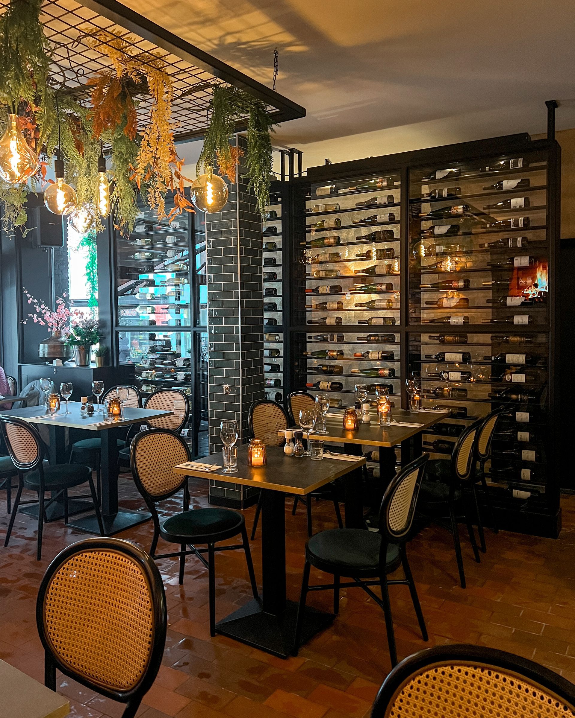 Een restaurant met tafels en stoelen en een muur vol wijnflessen.