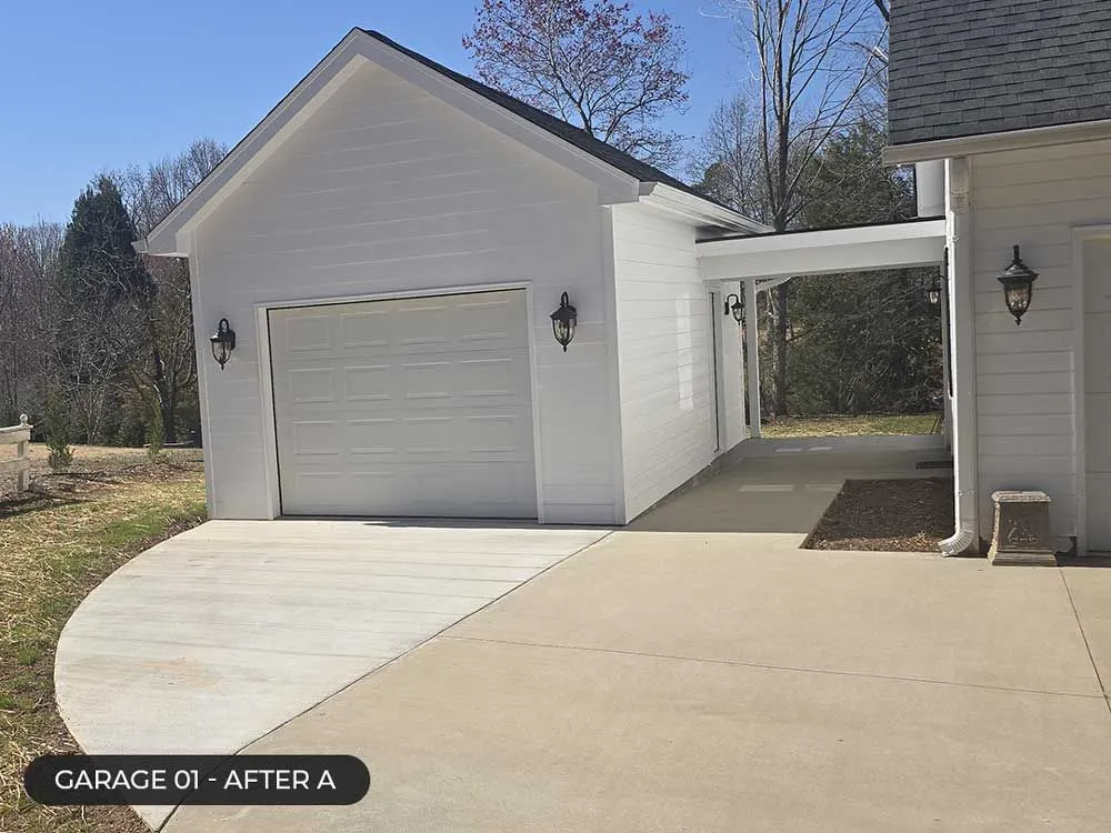 White detached garage with new concrete driveway and side walkway under a clear sky