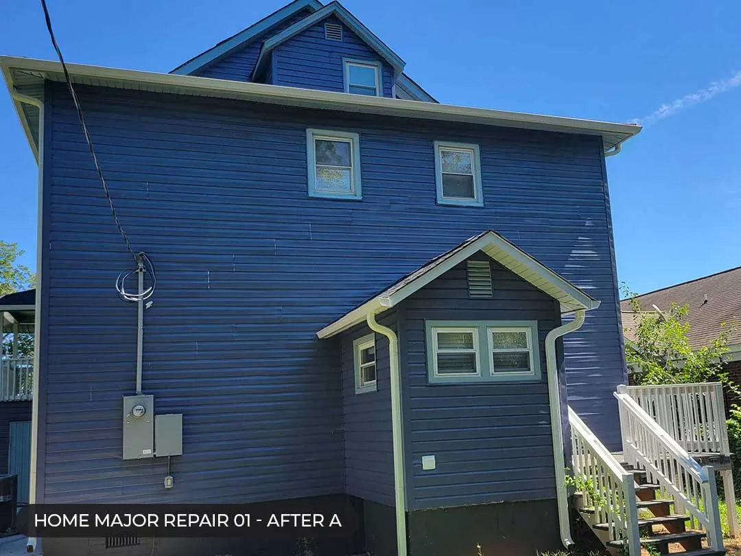 Blue house exterior with a small porch, white trim, and side stairs under a clear sky