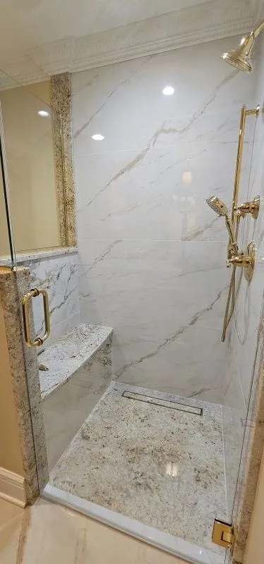 Glass shower enclosure with marble tile walls, bench, and gold hardware