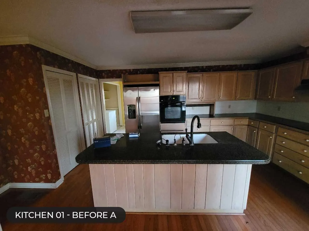 Kitchen with wood cabinets, black countertop island, and white paneled lower cabinets in a home interior.