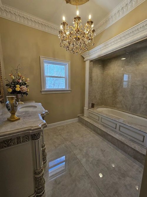 Elegant marble bathroom with gold chandelier, ornate vanity, and glass-enclosed shower