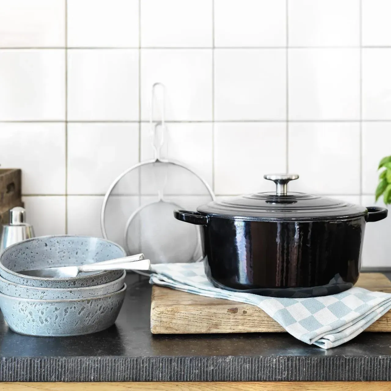 Een zwarte pot staat op een houten snijplank naast een stapel kommen.