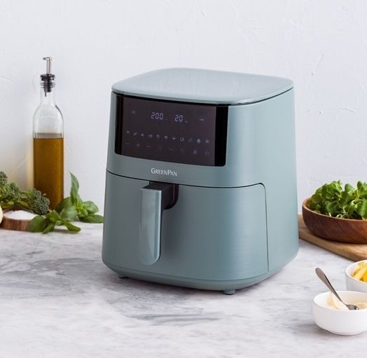 Een blauwe airfryer staat op een aanrecht naast groenten