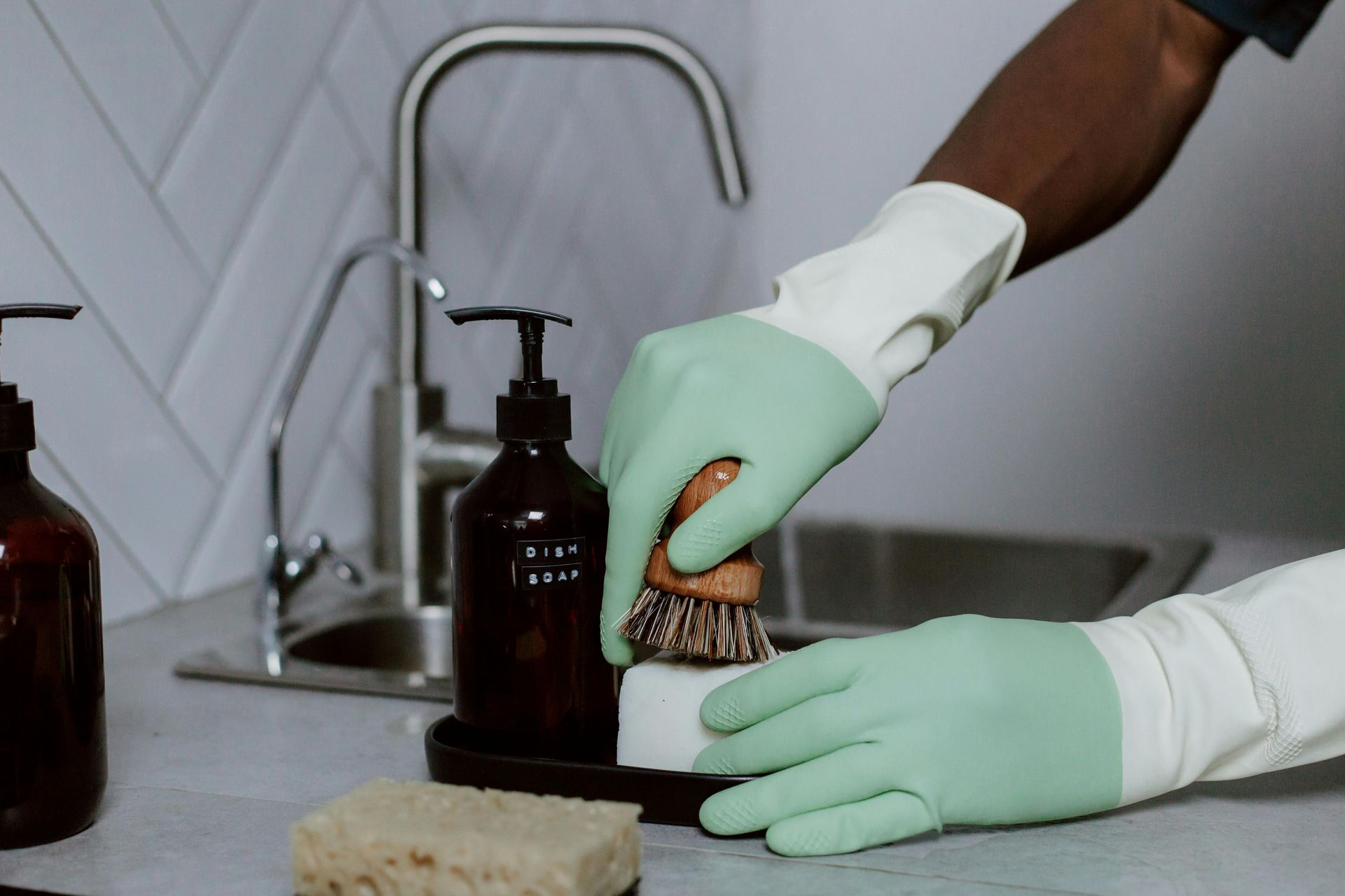Een persoon met groene handschoenen maakt een gootsteen schoon met een spons en een borstel.