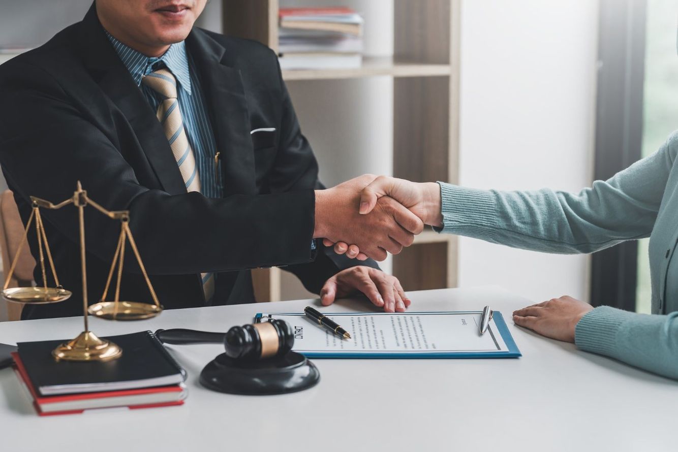 Lawyer shakes hands with a client over a contract; gavel and scales of justice on the desk.