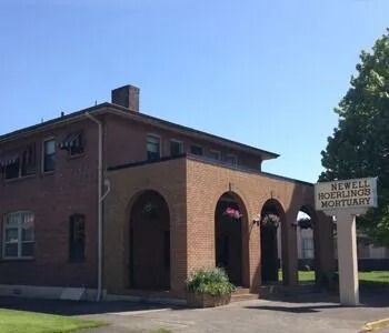 Brick funeral home building with arched entrances and a sign reading “Newell Funeral Mortuary”