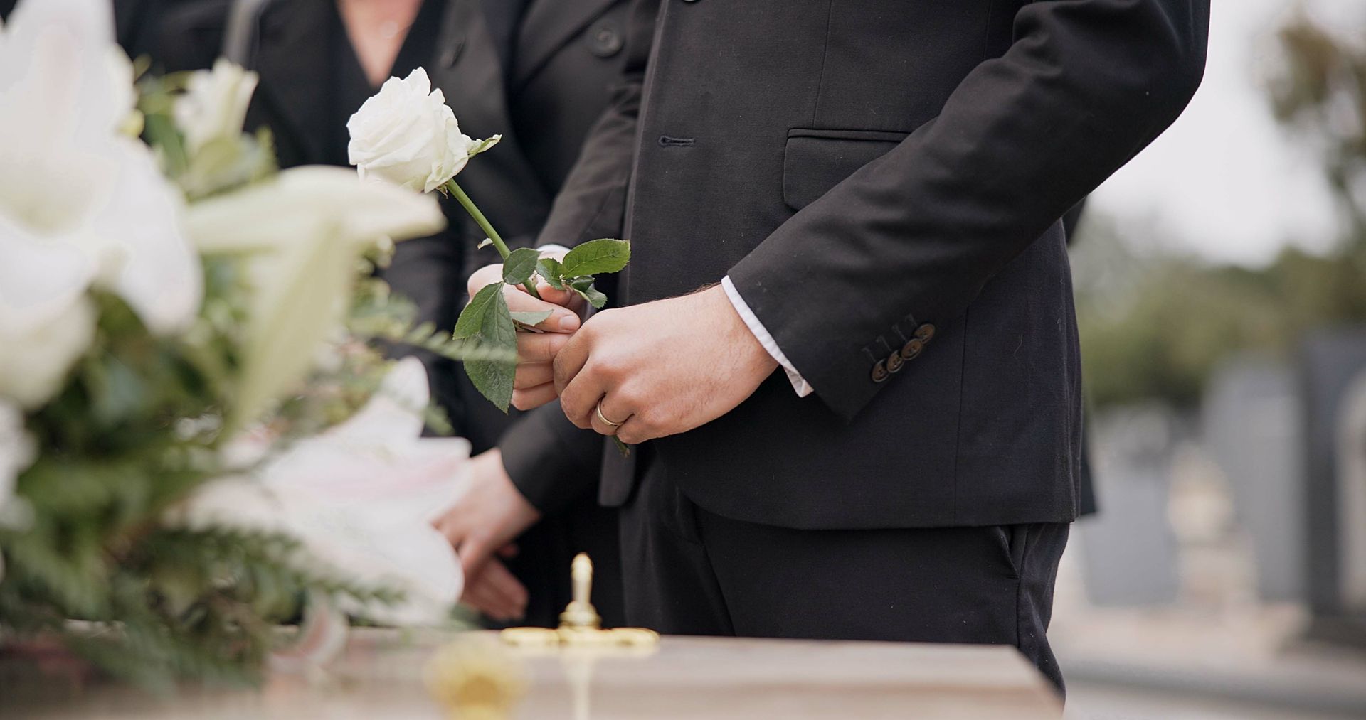 Person in a black suit holding red and white flowers at a graveside memorial