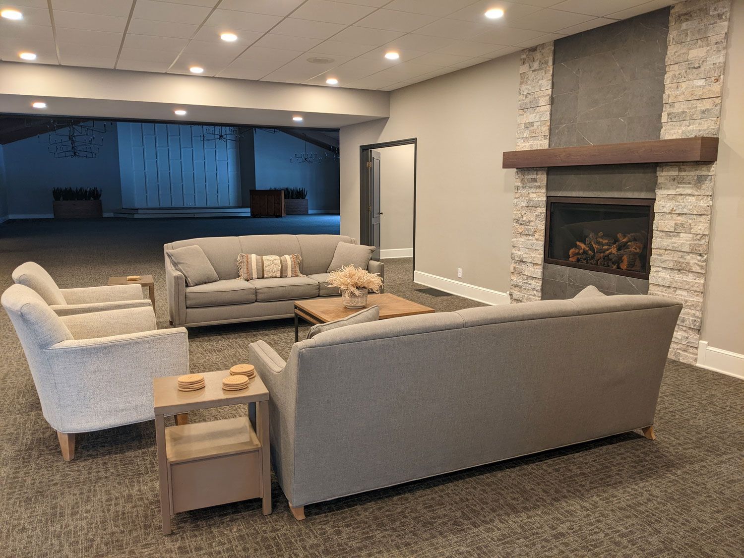 A seating area with gray sofas and chairs, a wood coffee table, and a stone fireplace in a neutral-toned room.