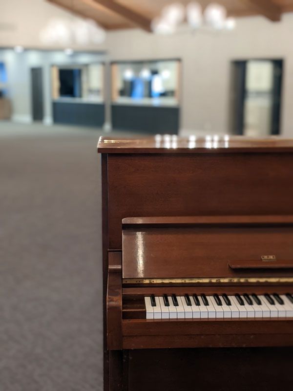 A brown upright piano stands in the foreground of a large, carpeted, and out-of-focus event space.