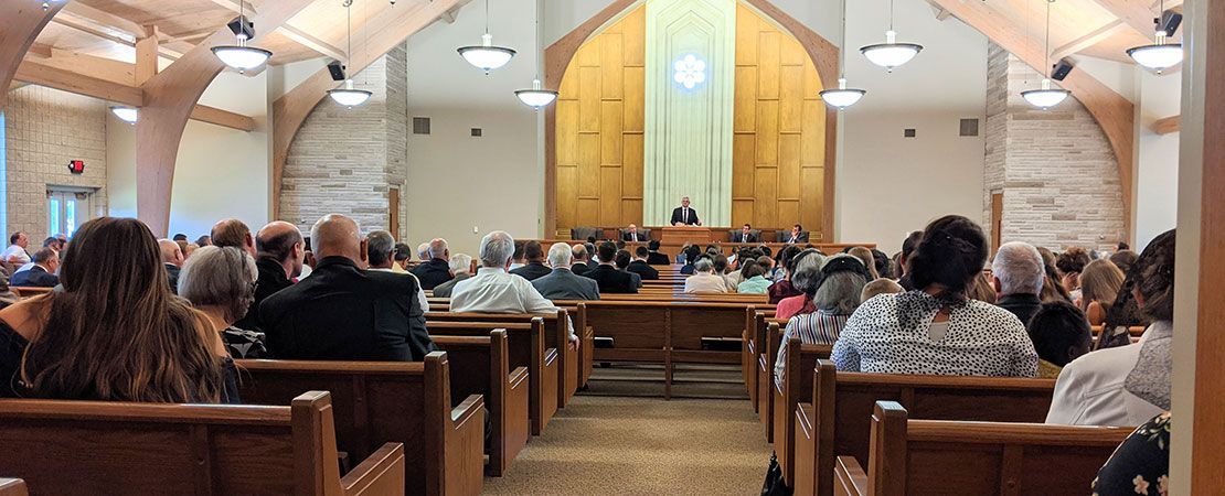 A perspective from the back of a wood-paneled church, facing a congregation seated in pews during a service.